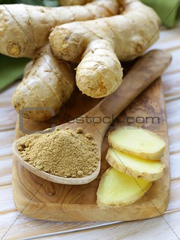 ground ginger in a wooden spoon, fresh root in the background