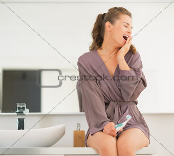 Young woman with toothbrush yawning