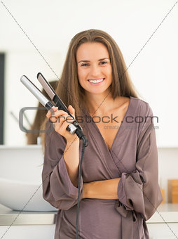 Portrait of happy young woman with hair straightener in bathroom