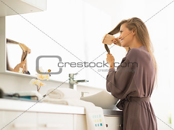 Young woman combing hair in bathroom