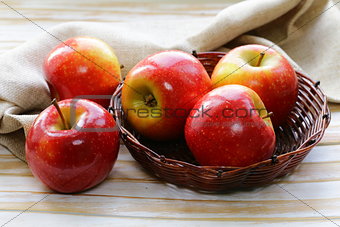 Red ripe apples in a wicker basket on a wooden table