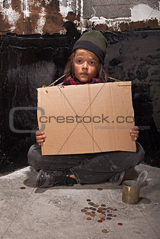 Poor beggar boy on the street with a cardboard sign