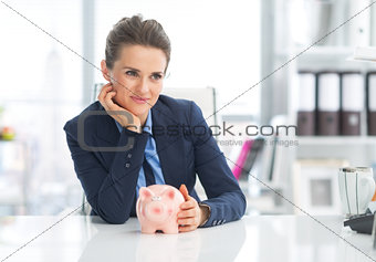 Thoughtful business woman with piggy bank