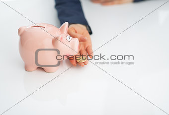 Closeup on business woman feeding piggy bank with coin