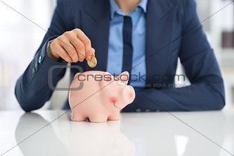 Closeup on business woman putting coin into piggy bank