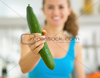 Closeup on happy young woman in kitchen showing cucumber