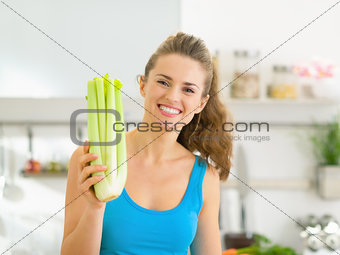 Happy young woman showing fresh celery in kitchen