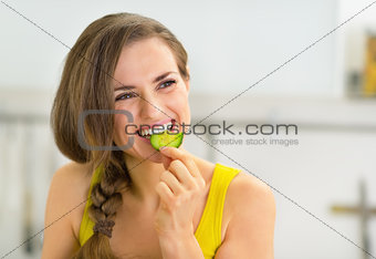 Portrait of young woman eating cucumber in kitchen