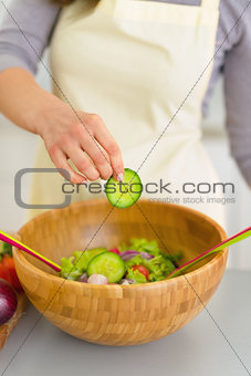 Closeup on young woman adding cucumber in salad
