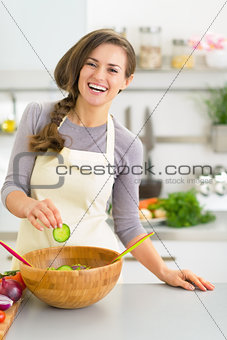 Happy young woman making salad in kitchen