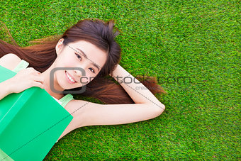 smiling girl student  laying down  on a meadow with books