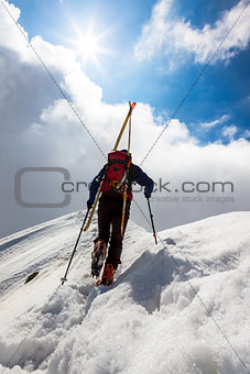  Ski mountaineer walking up along a steep snowy ridge with the s