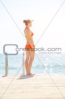Full length portrait of young woman standing on bridge and looki