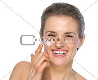 Happy young woman applying creme on face