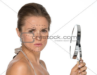 Concerned young woman with plastic surgery marks and mirror