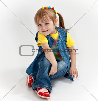 little girl in jeans and sandals is sitting on the floor