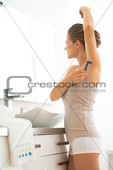 Young woman shaving armpit in bathroom