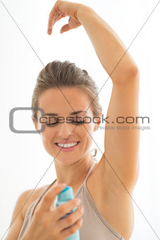 Happy young woman applying deodorant on underarm