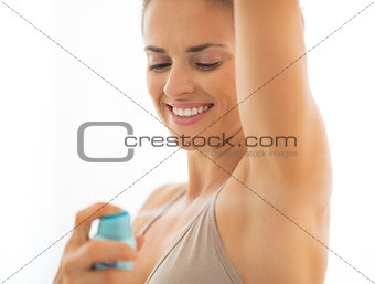 Happy young woman applying deodorant on underarm