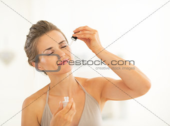 Portrait of young woman applying cosmetic elixir in bathroom