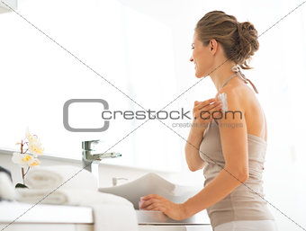 Young woman applying cream on shoulder in bathroom