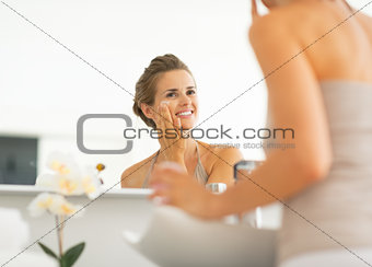 Happy young woman applying cream in bathroom