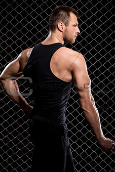 Guy showing his muscles on fence background
