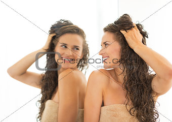 Happy young woman with long wet hair looking in mirror