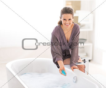 Happy young woman adding bath salt in bathtub