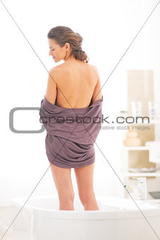 Young woman standing in bathtub. rear view