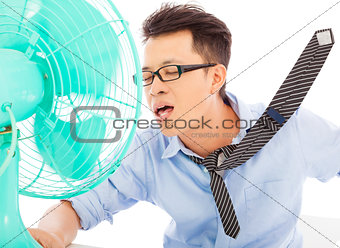 Young man cooling face under wind of fan