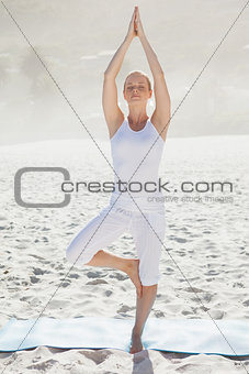 Calm woman standing in tree pose on beach