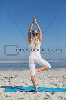 Blonde woman standing in tree pose on beach