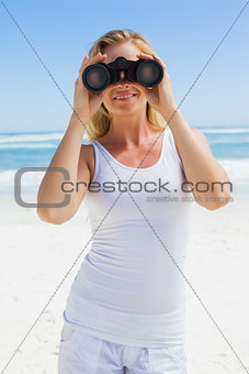 Blonde looking through binoculars on the beach