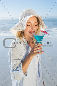 Smiling blonde relaxing by the sea sipping cocktail