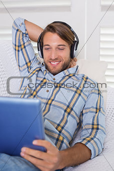 Casual smiling man lying on couch listening to music on tablet pc
