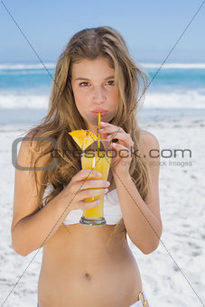 Pretty blonde in white bikini sipping cocktail on the beach