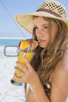Pretty smiling blonde in bikini sipping cocktail on the beach