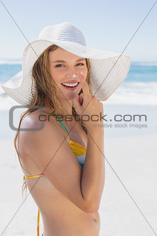 Beautiful girl putting spf on nose on the beach smiling at camera