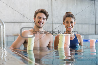 Man and woman standing with foam rollers in the pool