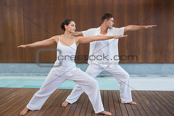 Peaceful couple in white doing yoga together in warrior position