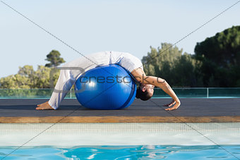 Peaceful brunette in cobra pose over exercise ball poolside