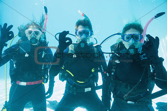 Friends on scuba training submerged in swimming pool looking to camera