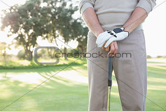 Mid section of golfer standing with club