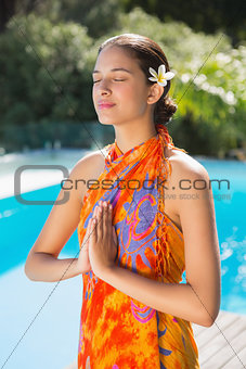 Brunette in sarong meditating by the pool