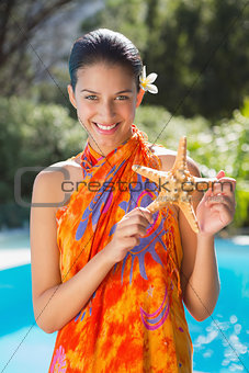 Smiling brunette in sarong showing starfish to camera