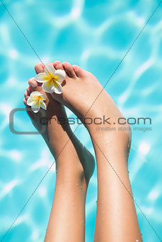 Feet dangling over swimming pool with flowers