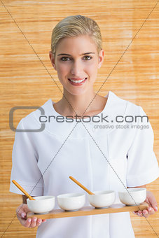 Smiling beauty therapist holding tray of treatments