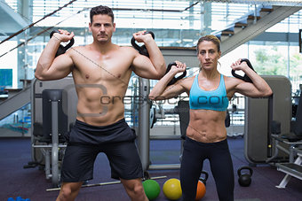 Bodybuilding man and woman lifting kettlebells looking at camera