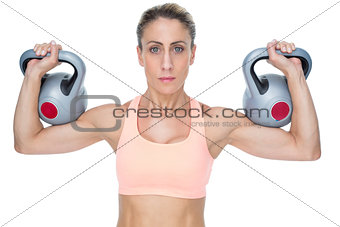 Serious female crossfitter lifting kettlebells looking at camera